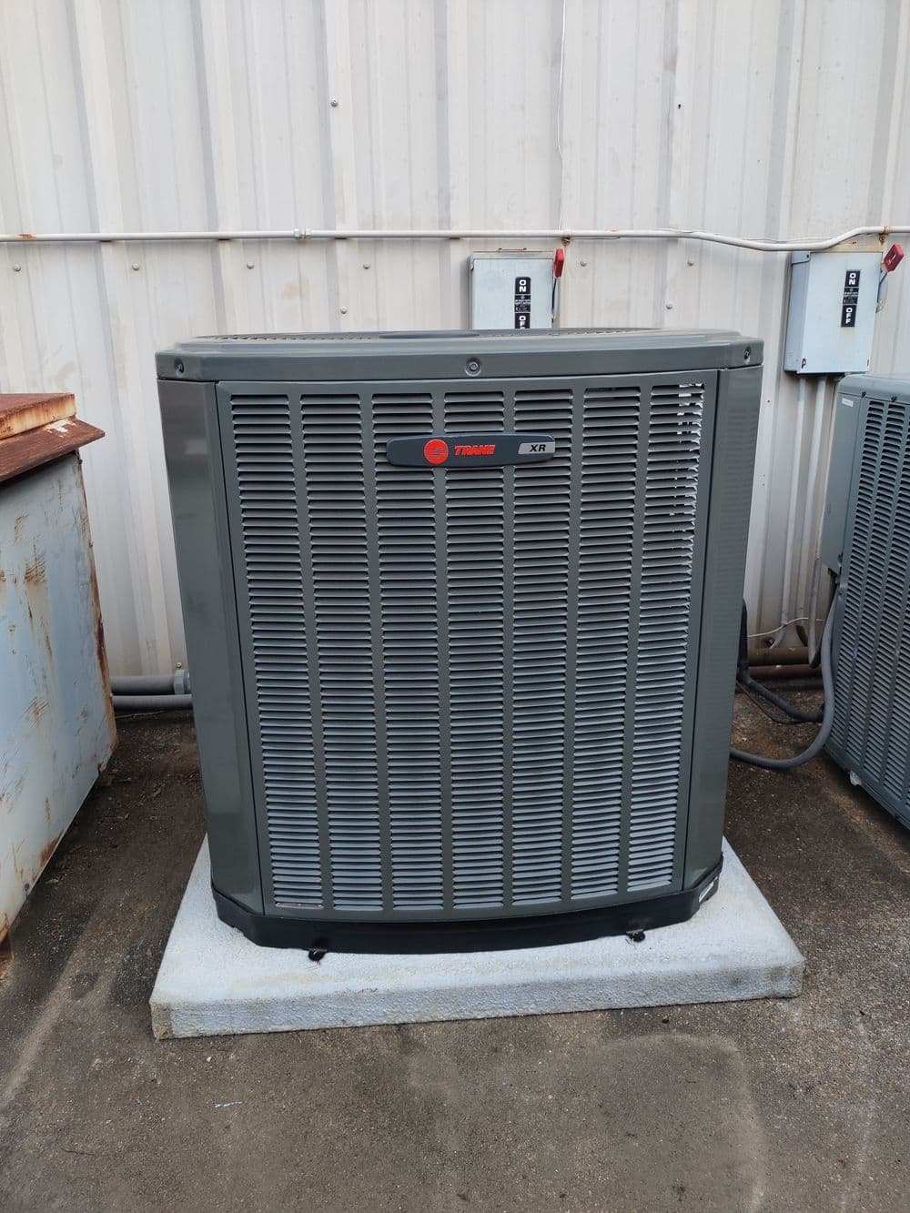 Trane outdoor air conditioning unit on concrete pad, gray color, with ventilation fins.